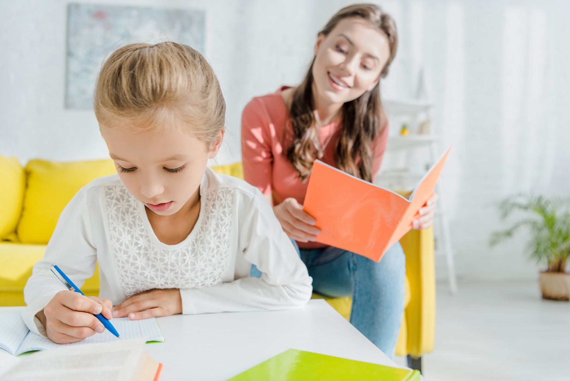 selective focus of cute child studying near attractive babysitter at home